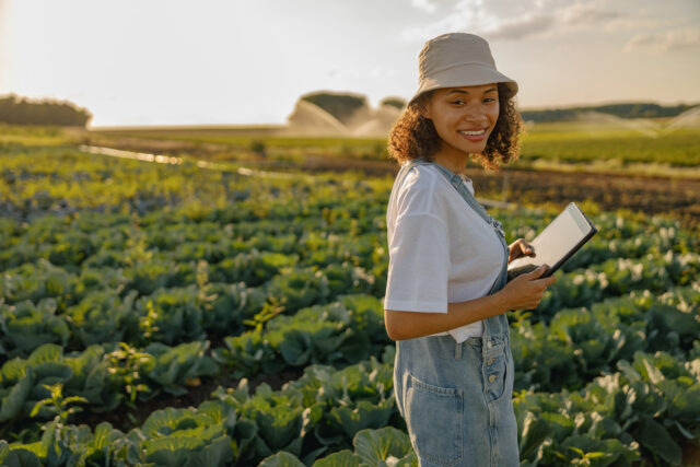 Smiling woman farmer work on digital tablet standing on cabbage field. Agricultural business concept Bayer lanza LEGADO 2026: busca startups que transformen la salud y la alimentación en América Latina